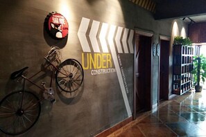 Un pasillo con una bicicleta apoyada en la pared, un letrero que dice 'UNDER CONSTRUCTION' y una puerta que da a otra habitación.