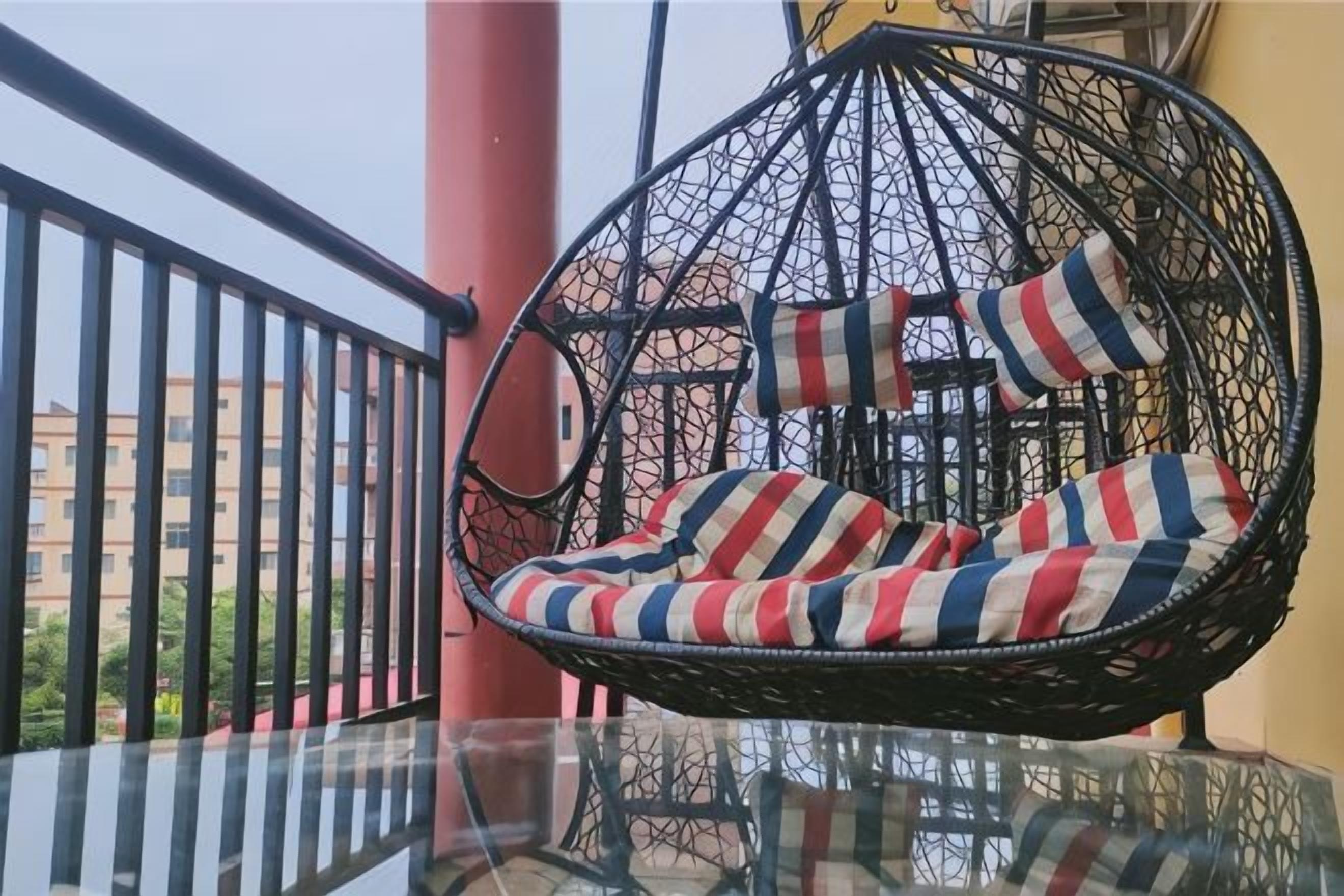 A hanging chair with striped cushions on a balcony with a glass table.