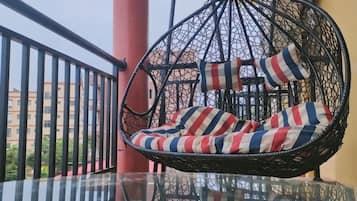 A hanging chair with striped cushions on a balcony with a glass table.