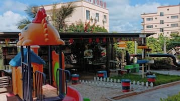 Un terrain de jeux avec un toboggan et des structures d’escalade, entouré d’une clôture et de palmiers.