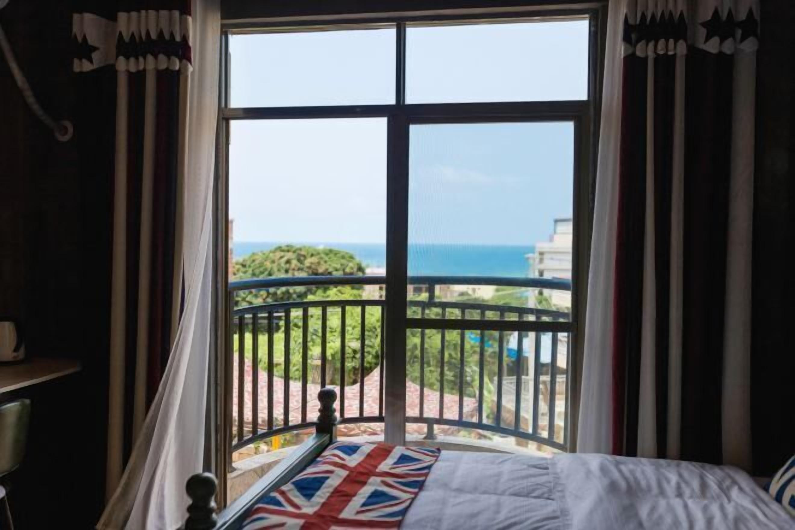 Une pièce dotée d’une grande fenêtre, d’un balcon avec une rambarde en métal et d’un lit agrémenté d’un coussin orné du drapeau Union Jack.