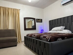 A bedroom with a bed, a sofa, a mirror, and an air conditioning unit.