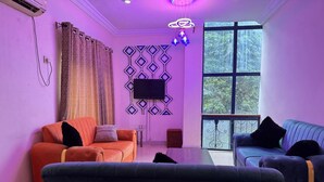 A living room with two sofas, a TV, and a window with a view of greenery. - Doris O Hotel  (Calabar)