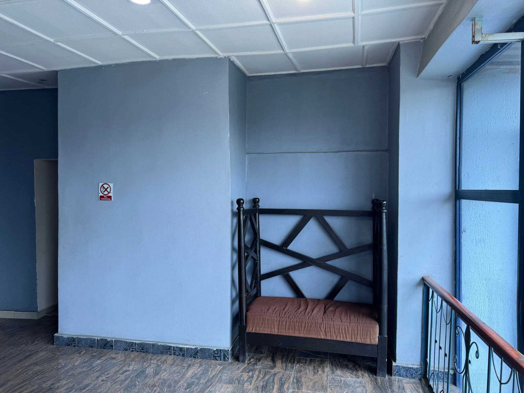 Een kamer met een bed tegen een blauwe muur, een rookvrij bord en een trap met een metalen leuning.