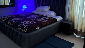A modern bedroom with a bed, bedside table, lamp, air conditioning unit, and a window with curtains. - Doris O Hotel  (Calabar)