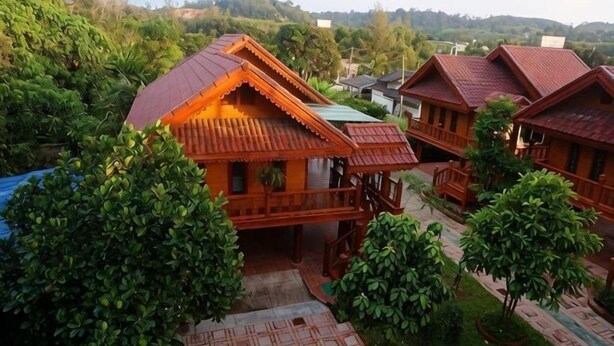 Un ensemble de chalets en bois dotés de balcons, entourés d’une végétation luxuriante et avec des collines en arrière-plan.