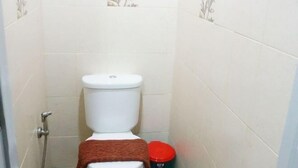 Une petite salle de bain étroite, équipée de toilettes, d’une douche et d’une poubelle.