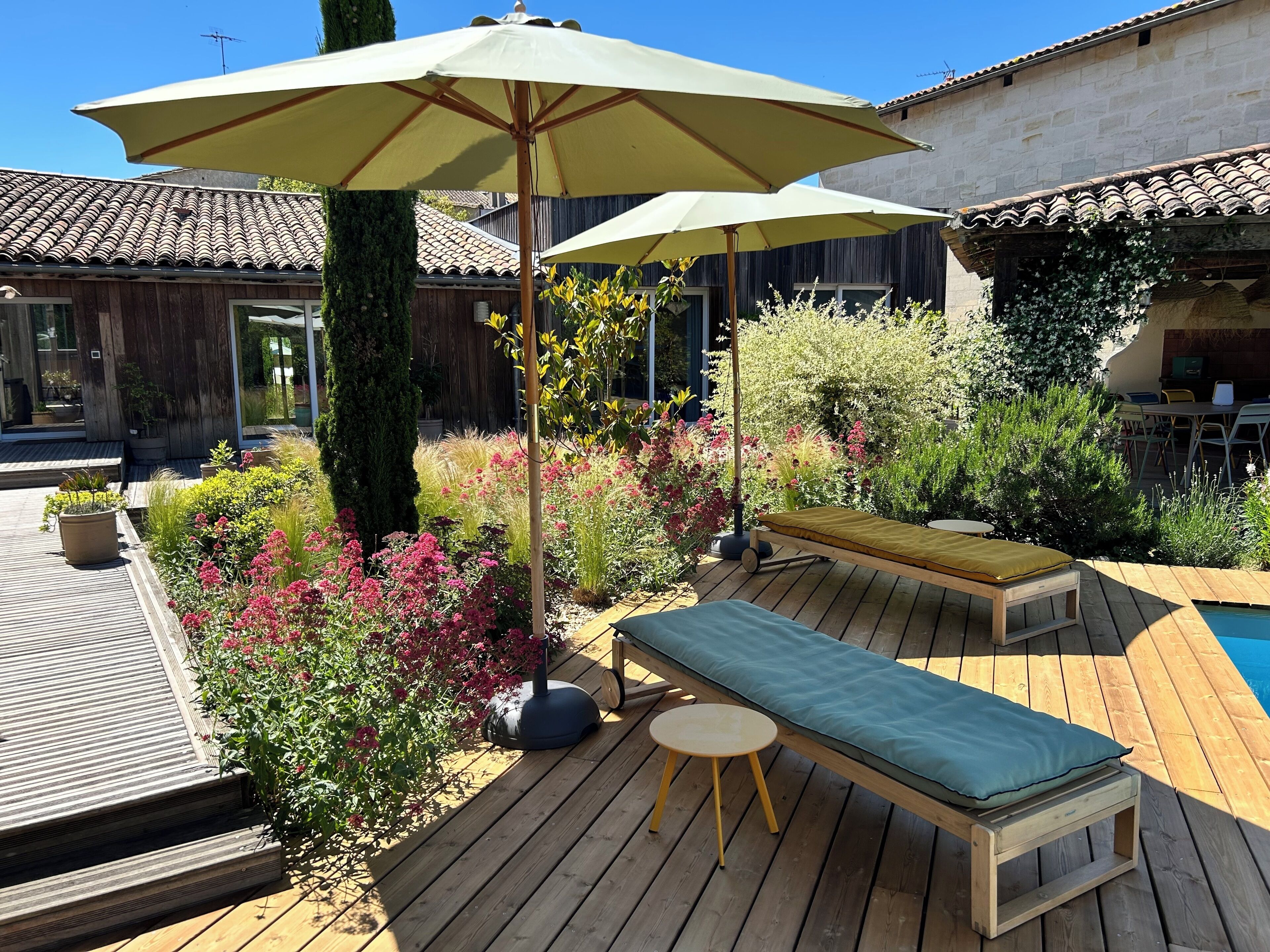 A wooden deck with a pool, outdoor seating, and a garden with various plants and flowers.