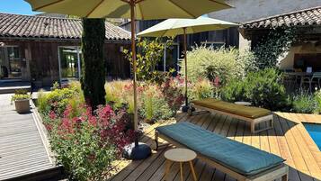 A wooden deck with a pool, outdoor seating, and a garden with various plants and flowers.