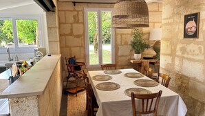 A rustic dining area with a stone wall, a hanging wicker lamp, and a view of greenery outside. - La Bohème: Gîte with swimming pool 20 minutes from Saint-Emilion. Dogs welcome. (Galgon)