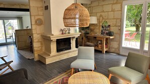 A living room with a fireplace, two chairs, a sofa, a dining table, and a large window. - La Bohème: Gîte with swimming pool 20 minutes from Saint-Emilion. Dogs welcome. (Galgon)