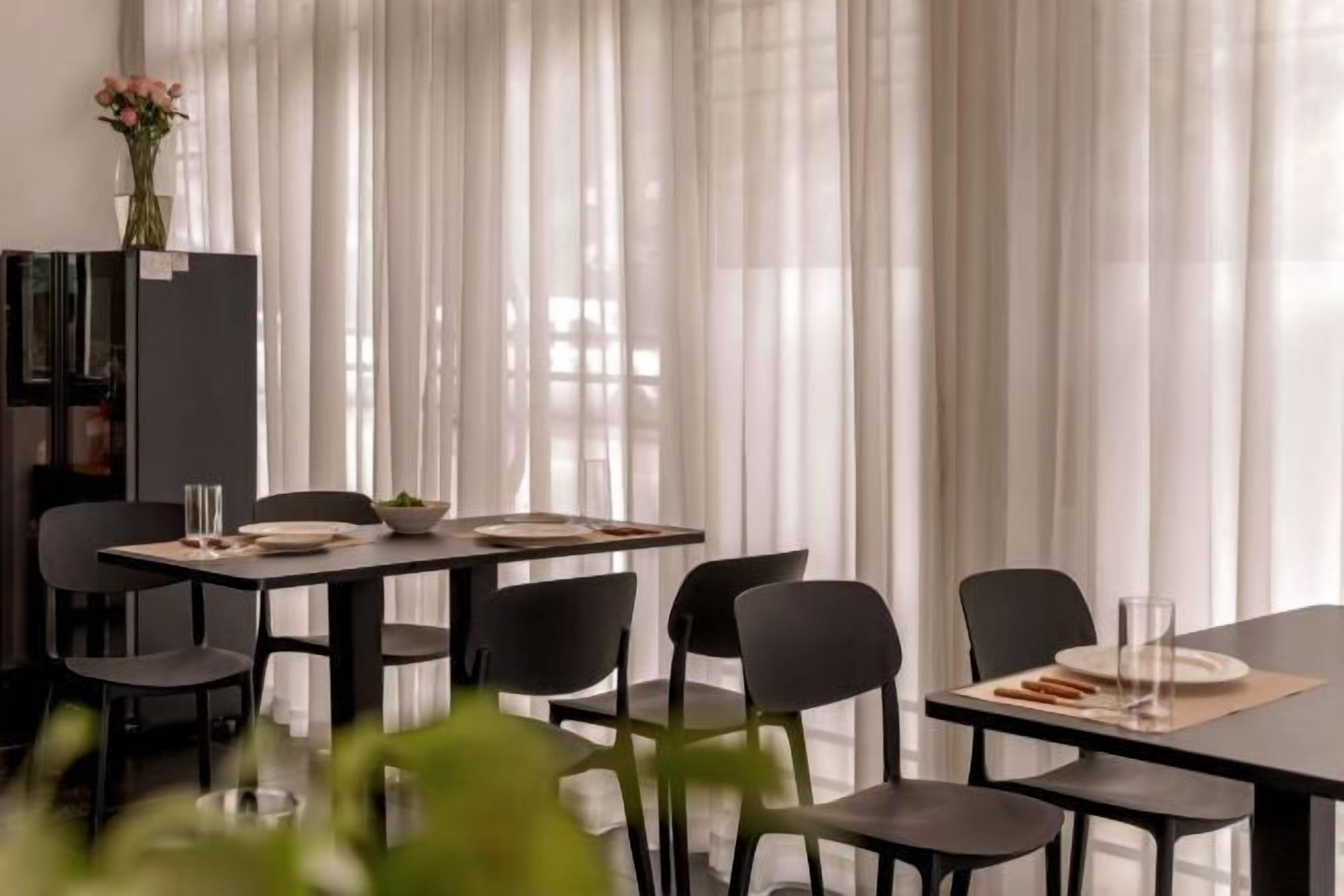 A dining area with a table set for two, chairs, a vase with flowers, and a bookshelf.