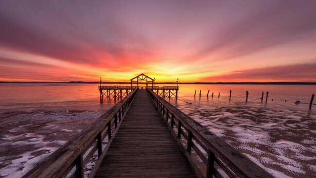 A wooden pier leading to a structure at sunset.