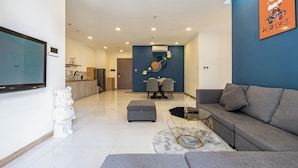 Ein modernes Wohnzimmer mit einem grauen Sofa, einem Couchtisch und einem an der Wand montierten Fernseher. Im Hintergrund befindet sich ein Essbereich mit Tisch und Stühlen.