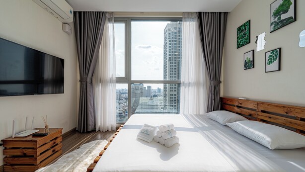 Ein modernes Hotelzimmer mit einem großen Bett, einem Flachbildfernseher, einem Holfnachtkästchen und Blick auf die Stadt durch große Fenster.
