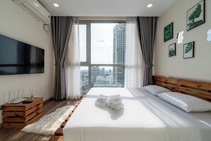 Habitación de hotel moderna con una cama grande, un televisor de pantalla plana, una mesita de madera y vistas de la ciudad a través de ventanas amplias.