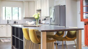 Een moderne keuken met een centraal eiland, twee gele stoelen en een bloevas.