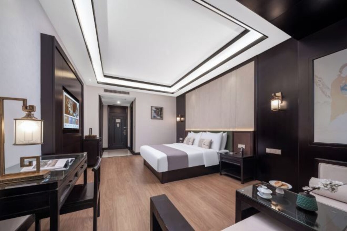 Una habitación de hotel moderna con cama, mesitas de noche, escritorio y un amplio ventanal.