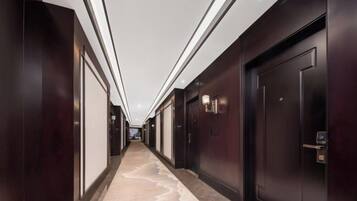 A long, narrow hallway with dark wooden doors and walls, recessed lighting, and a marble-like floor.