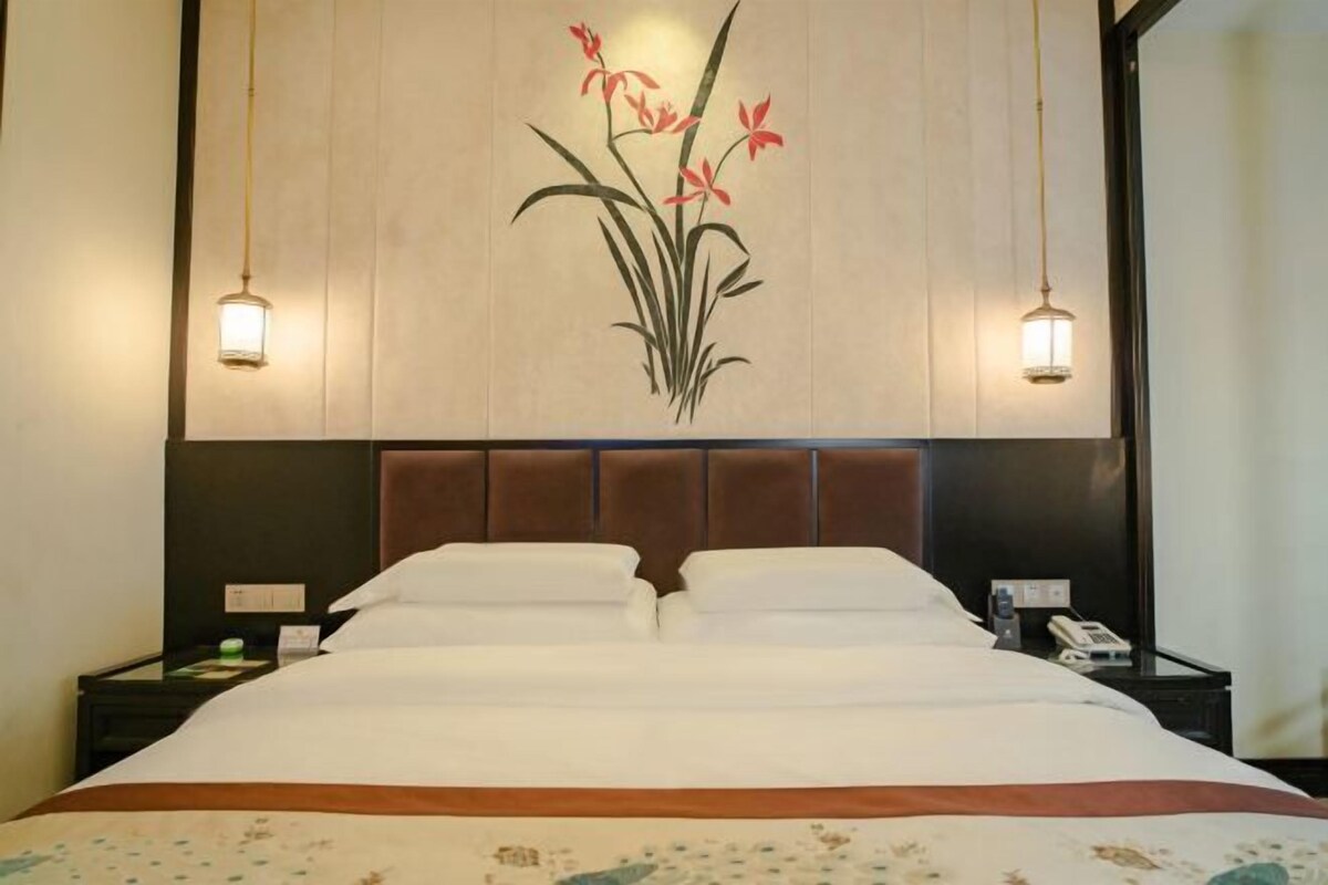 Une chambre d’hôtel avec un grand lit, deux tables de chevet, une œuvre d’art représentant des fleurs accrochée au mur, et deux lampes murales.