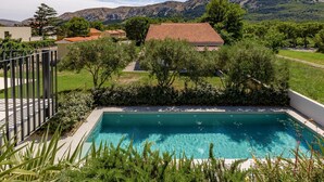 A rectangular swimming pool with clear blue water, surrounded by lush greenery and a view of mountains in the background. - Pool Apartment Sapore Di Mare 3 (Baska)