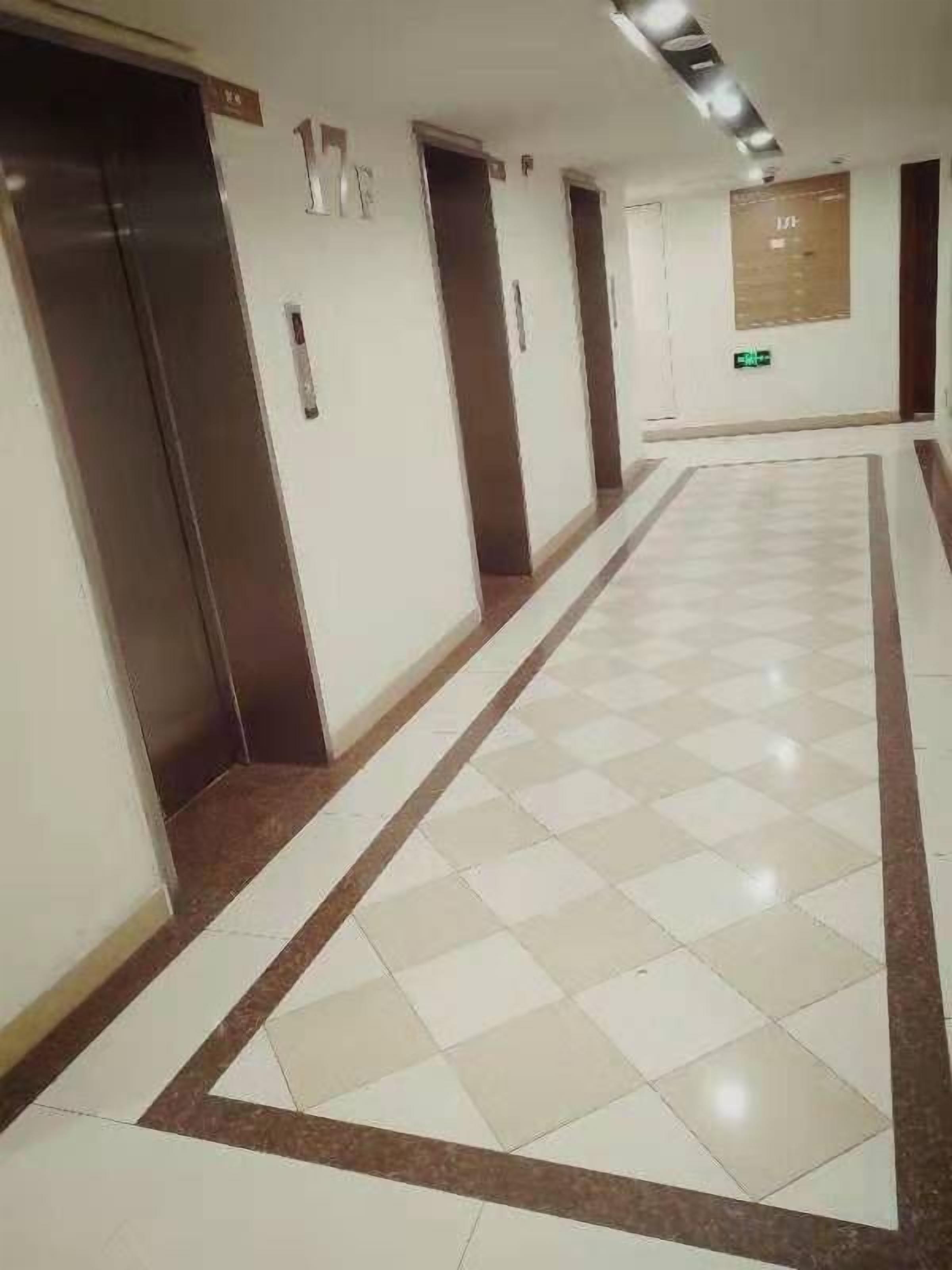 A corridor with a checkered floor, doors marked with numbers, and a bulletin board on the wall.