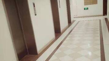 A corridor with a checkered floor, doors marked with numbers, and a bulletin board on the wall.