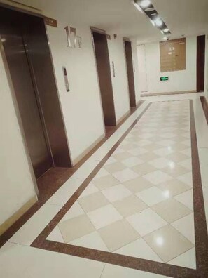 A corridor with a checkered floor, doors marked with numbers, and a bulletin board on the wall. - Jiaozhou Haiyue Apartment Hotel (Jiaozhou)