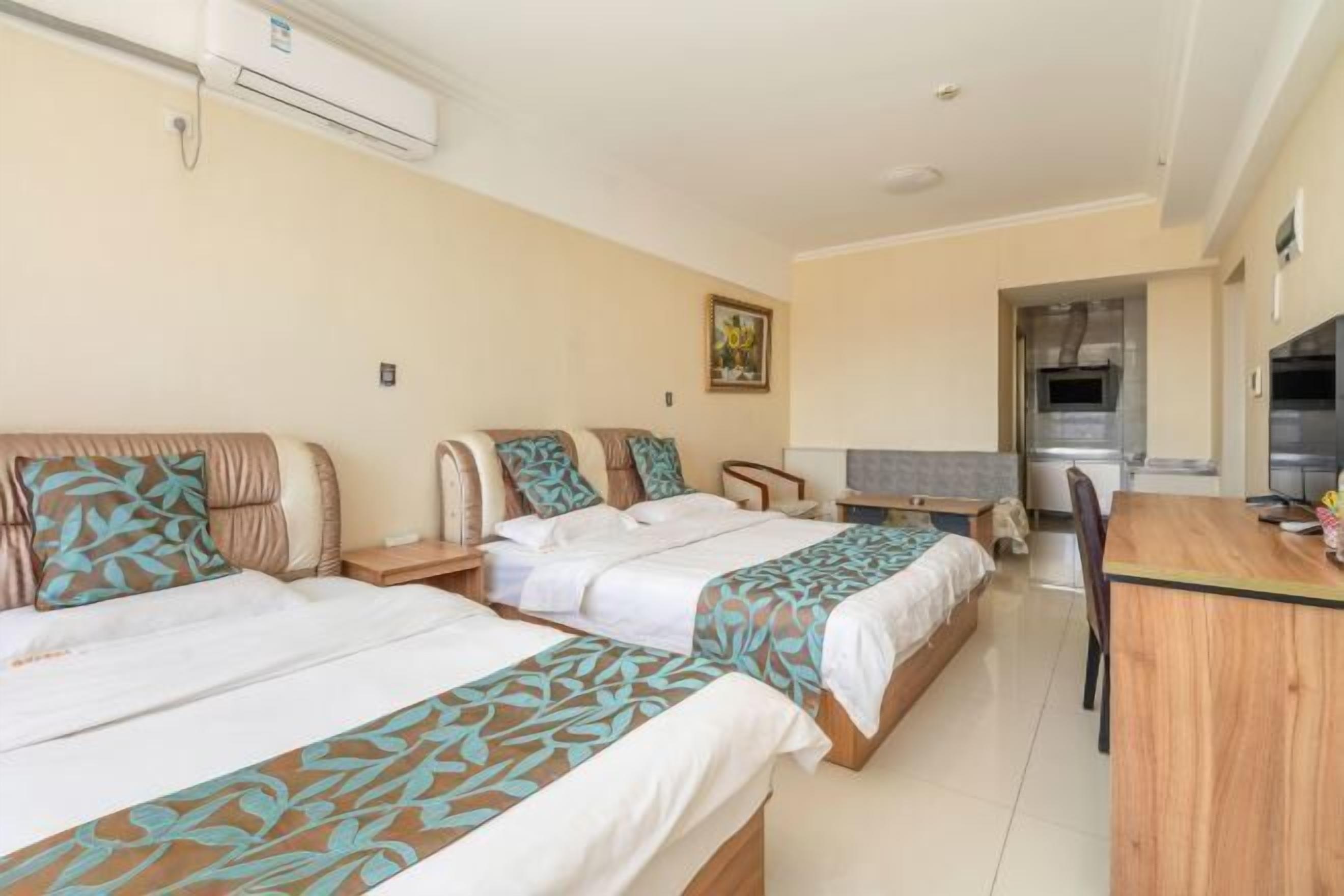 A hotel room with two beds, a dining table, a kitchenette, and a ceiling-mounted air conditioner.