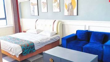Une chambre d’hôtel avec un lit, un canapé bleu, une petite table et des œuvres d’art accrochées au mur.