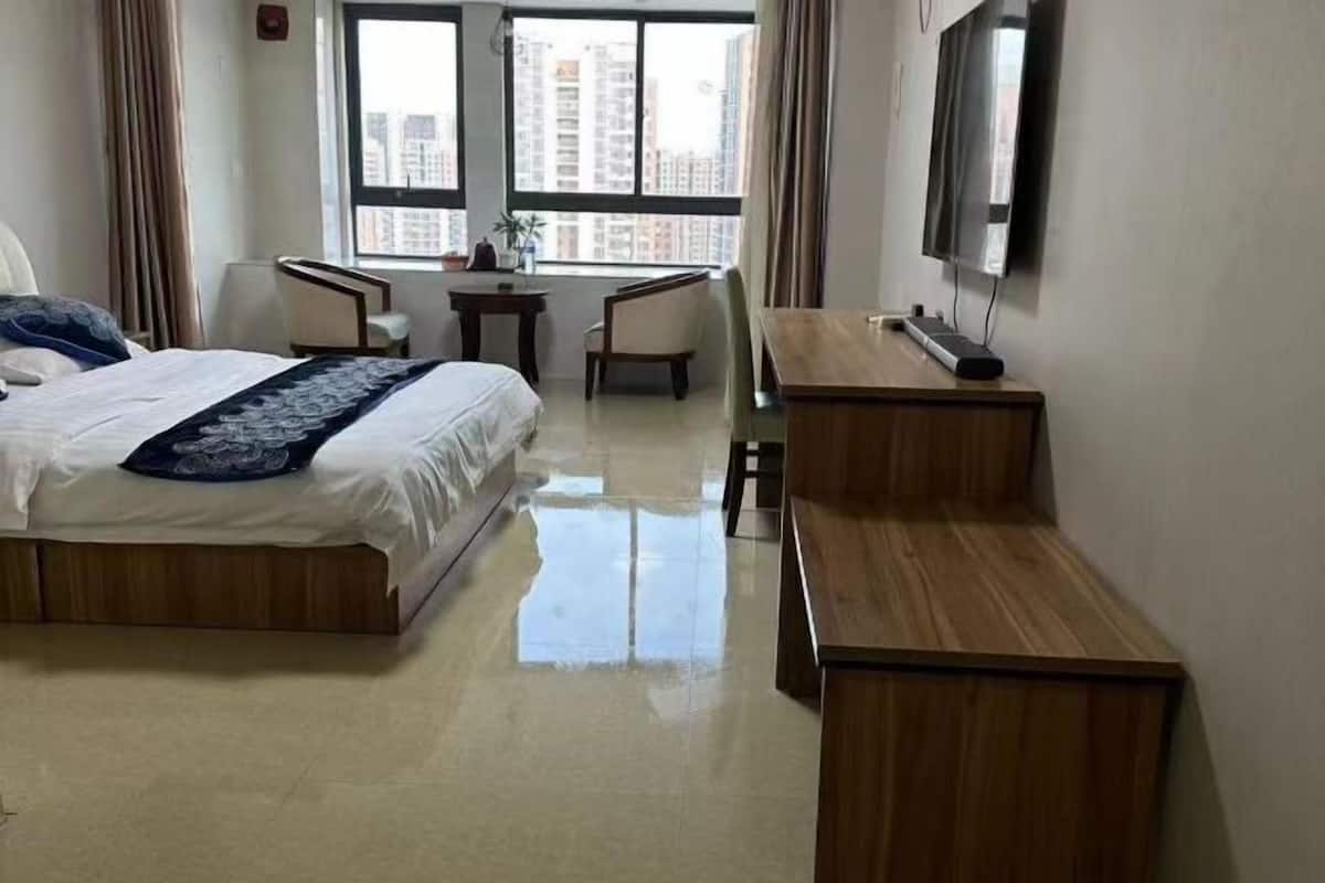 Une chambre d’hôtel avec un lit, un bureau, une chaise, une télévision et une vue sur les bâtiments par la fenêtre.