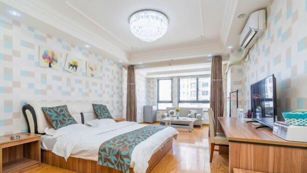 A modern hotel room with a large bed, a desk, a TV, and a window with curtains. - Jiaozhou Haiyue Apartment Hotel (Jiaozhou)