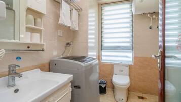 A bathroom with a sink, a washing machine, a toilet, and a window with blinds.
