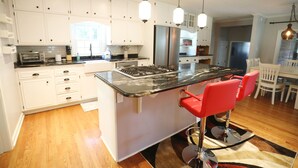 A modern kitchen with white cabinets, a stainless steel refrigerator, a gas stove, and red bar stools. - Purdue Bell Tower views, Central WL location, Walk 2 Purdue (West Lafayette)