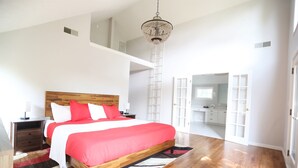 Une chambre avec un lit en bois, des murs blancs, un lustre et une vue sur la salle de bain.