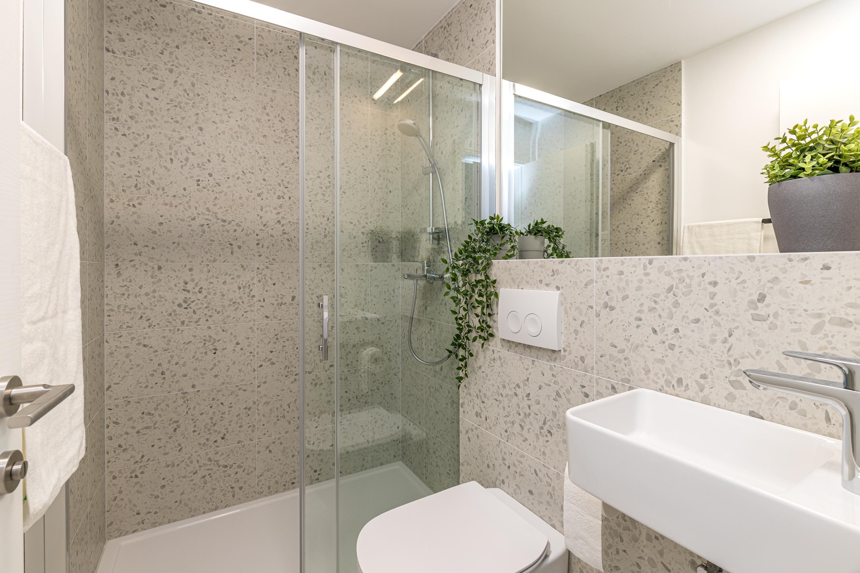 Un baño moderno con cabina de ducha de vidrio, inodoro blanco y lavamanos con espejo.