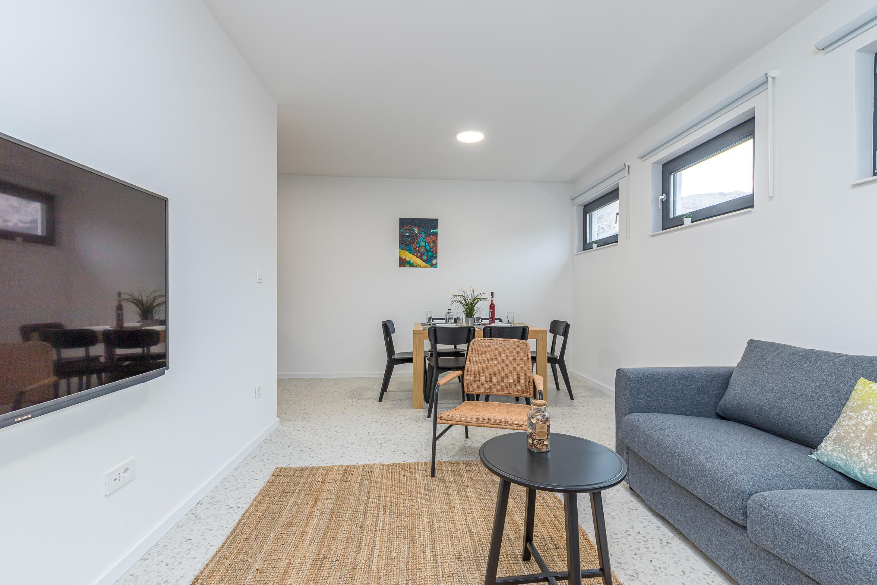 Een moderne woonkamer met een grijze bank, een kleine ronde tafel en een eethoek met een tafel en stoelen.