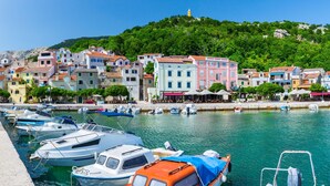 A marina with boats docked, a waterfront promenade, and colorful buildings in the background. - Pool Apartment Sapore Di Mare 4 (Baska)