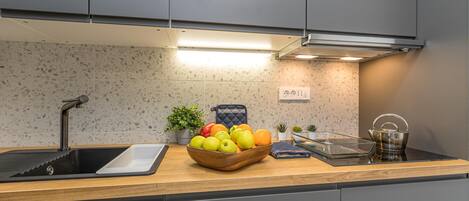 A modern kitchen with a granite countertop, a sink, a bowl of fruit, and a kettle.