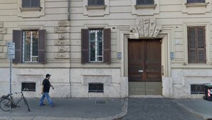 Un uomo che passa davanti a un edificio con un'imponente porta in legno e una facciata in pietra.