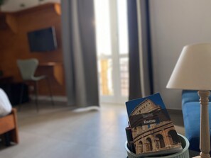 A hotel room with a bed, a chair, a lamp, and a view of a building through a window. - Cecilia B&B Roma (Rome)