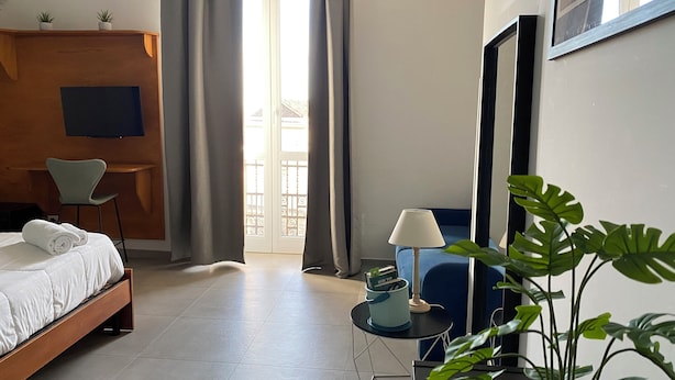 Una camera d'albergo con un letto, una scrivania, una sedia, una lampada e una pianta in vaso.