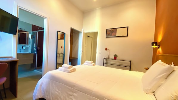 A hotel room with a bed, a desk, a chair, a bedside table with a lamp, and a mirror on the wall. - Cecilia B&B Roma (Rome)