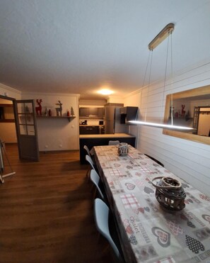 A compact kitchen with modern appliances, a dining area with a patterned tablecloth, and a mirror on the wall. - 100m from ski slopes, 3rd floor, swimming pool, sauna, hammam, balcony, fireplace or stove, tv (Val Thorens)