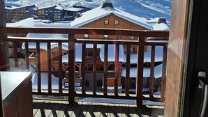 A wooden balcony with a view of snow-covered mountains and buildings. - 100m from ski slopes, 3rd floor, swimming pool, sauna, hammam, balcony, fireplace or stove, tv (Val Thorens)