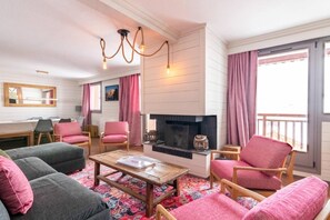 A cozy living room with a fireplace, comfortable seating, and a large window with curtains. - 100m from ski slopes, 3rd floor, swimming pool, sauna, hammam, balcony, fireplace or stove, tv (Val Thorens)