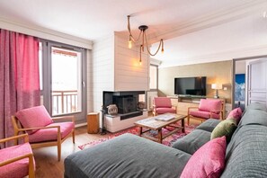 A modern living room with a fireplace, a television, and a balcony with red curtains. - 100m from ski slopes, 3rd floor, swimming pool, sauna, hammam, balcony, fireplace or stove, tv (Val Thorens)