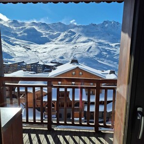 A wooden balcony with a view of snow-covered mountains and buildings. - 100m from ski slopes, 3rd floor, swimming pool, sauna, hammam, balcony, fireplace or stove, tv (Val Thorens)