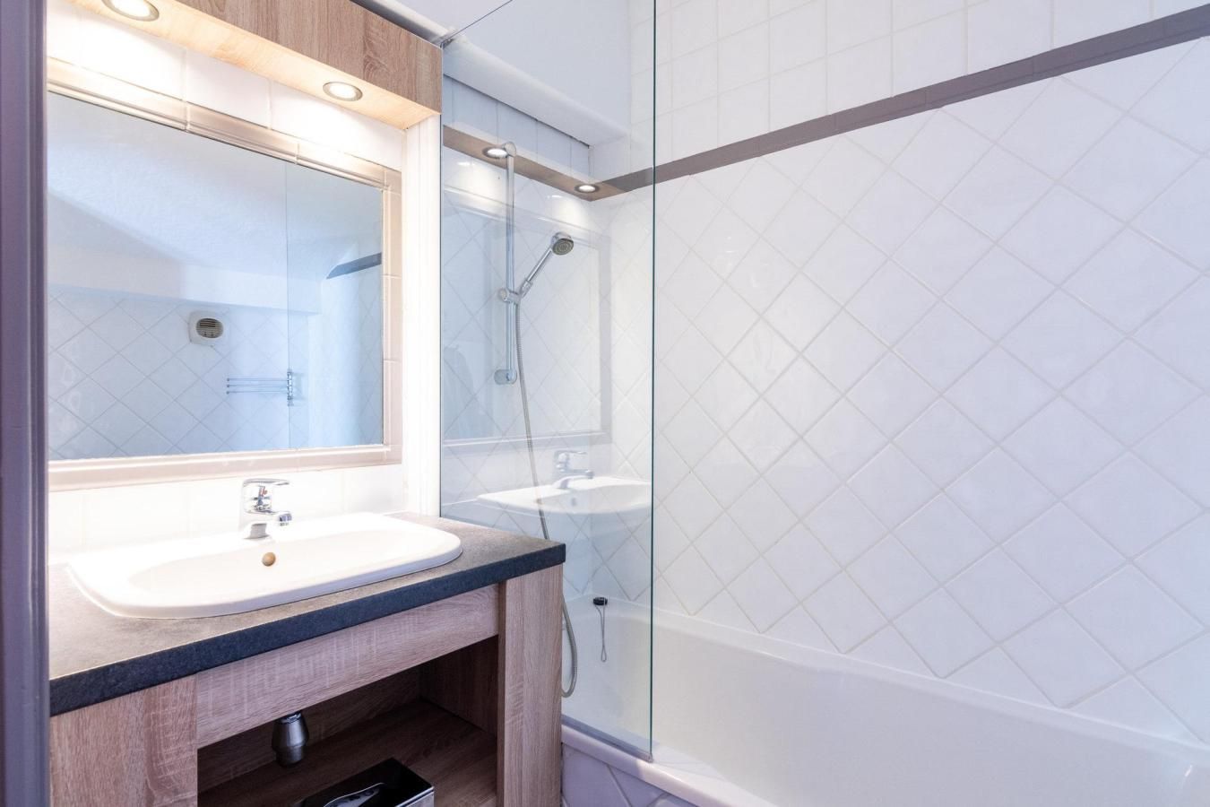 Une salle de bain moderne avec une douche à parois de verre, un lavabo blanc et un miroir au-dessus.