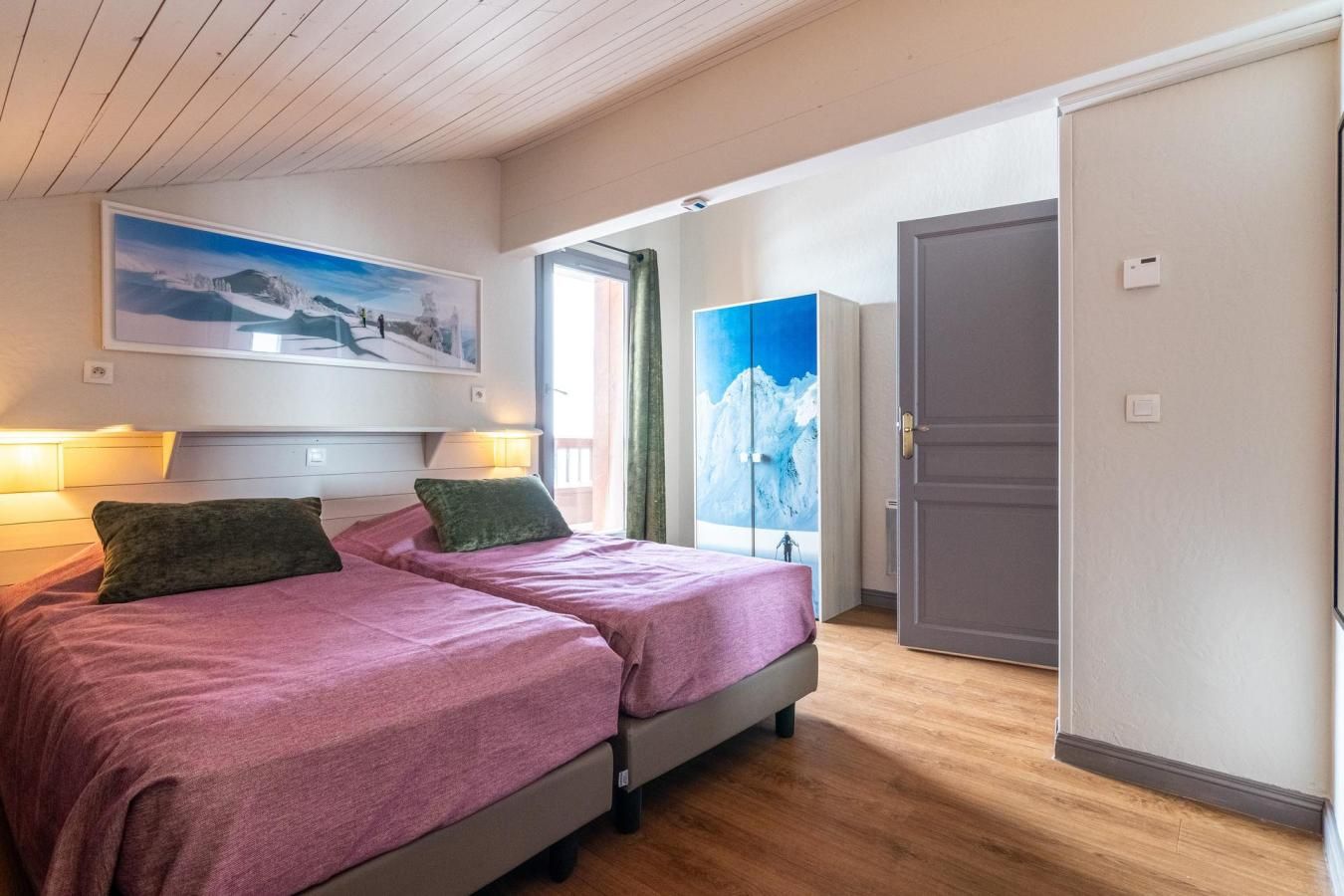 Ein Schlafzimmer mit zwei Betten, einem großen Fenster mit Blick auf die Berge und einer Tür zu einem anderen Raum.